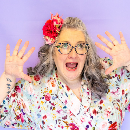 Vie n a floral dress, flowers in her hair, hands by her face looking aghast!