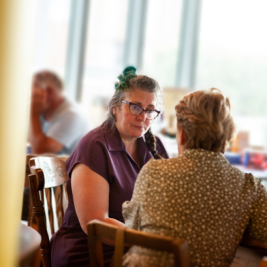 Vie sat with someone at a table, deep in discussion, during a 1:1 coaching session