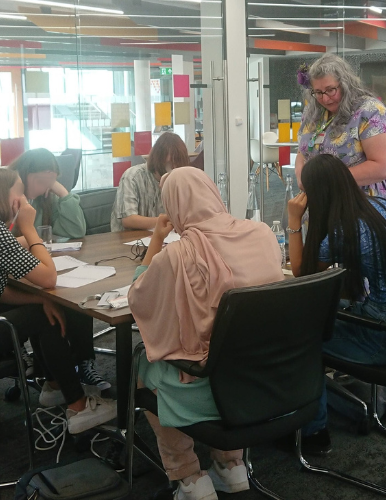 A group of individuals collaborating around a table, with one person facilitating a discussion.